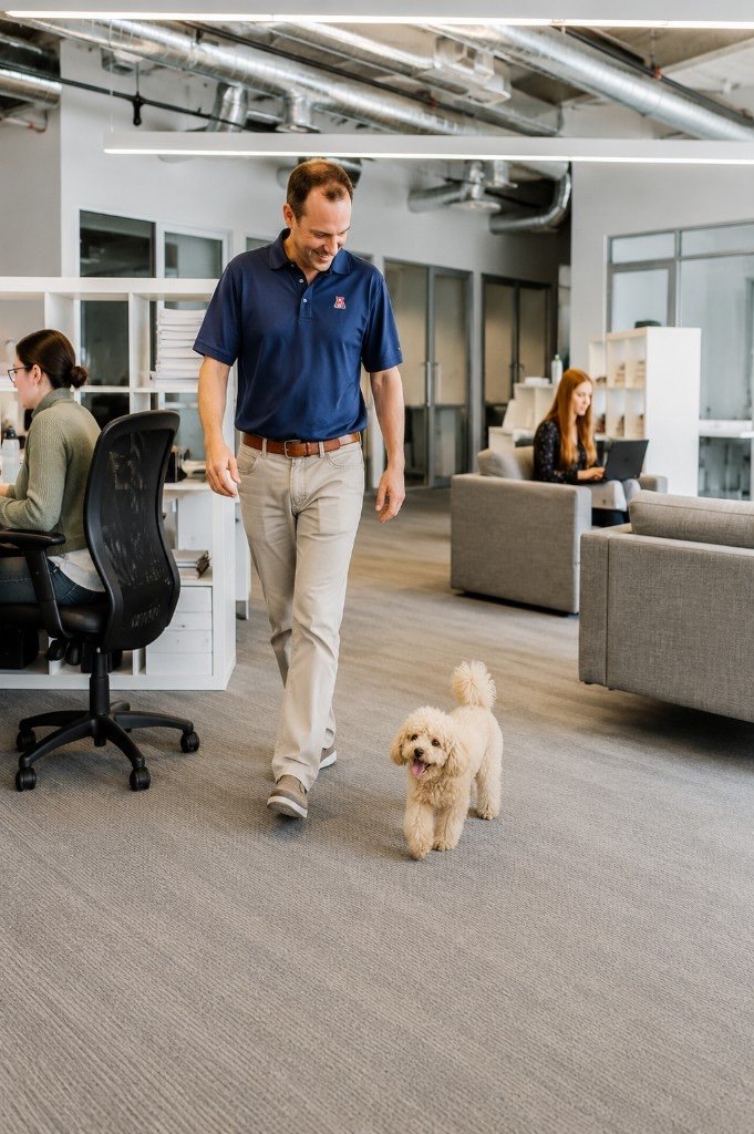 Man walking a poodle through an open-plan office